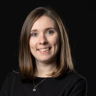 Eine junge Frau mit schulterlangen Haaren lächelt freundlich in die Kamera, vor einem dunklen Hintergrund.