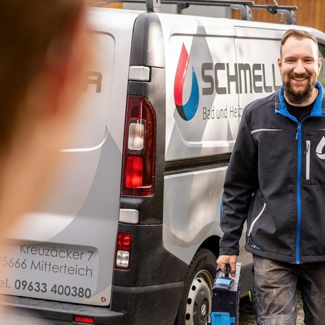 Ein Handwerker mit einem Werkzeug in der Hand steht vor einem Firmenfahrzeug und strahlt Zuversicht und Freundlichkeit aus.