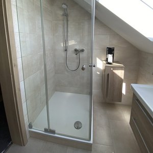 Eine moderne Dusche mit gläserner Abtrennung, hellen Fliesen und einem eleganten Duschkopf, die einladend wirkt.