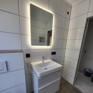 Das Bild zeigt ein stilvolles Waschbecken mit einem minimalistischen Design und einem großen, beleuchteten Spiegel darüber.