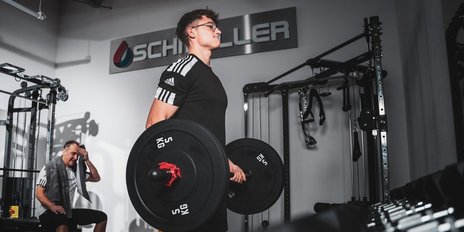 Der Athlet konzentriert sich auf das Heben von schweren Hanteln, während sein Trainingspartner eine Pause macht.