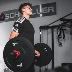 Der Athlet konzentriert sich auf das Heben von schweren Hanteln, während sein Trainingspartner eine Pause macht.