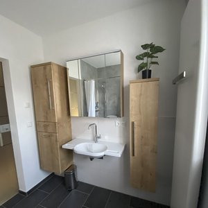 Ein modernes Badezimmer mit Holzschränken, einem Waschbecken und einem großen Spiegel, der den Raum reflektiert.